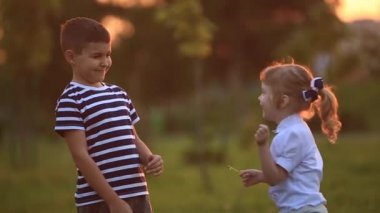 Küçük erkek ve kız çalıştırmak ve yürütmek. Karahindiba patlattılar. günbatımı