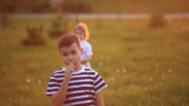 Menino e menina correm e brincam. Eles rebentam com o dente-de-leão. pôr do sol — Vídeo de Stock