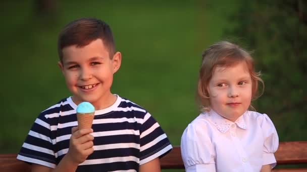 Mały chłopiec i dziewczynka siedzi na ławce i zjada lody — Wideo stockowe