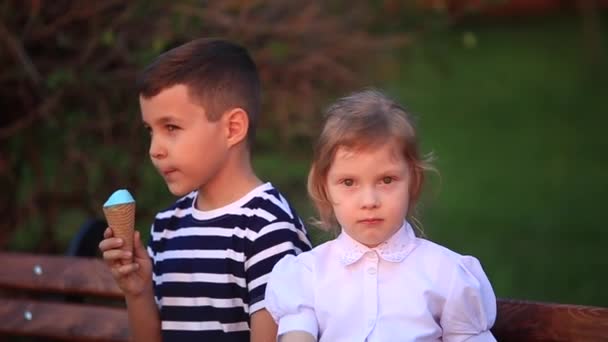Μικρό αγόρι και το κορίτσι να κάθεται στον πάγκο και να τρώει ένα παγωτό — Αρχείο Βίντεο