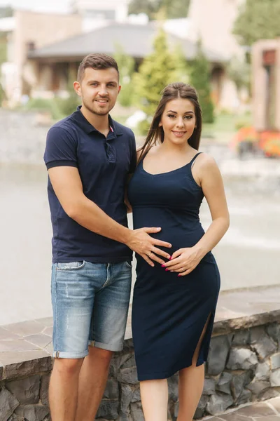 La mujer embarazada y su esposo se abrazan y sonríen. El hombre puso su mano de vientre de mujer embarazada. Seis meses de embarazo —  Fotos de Stock