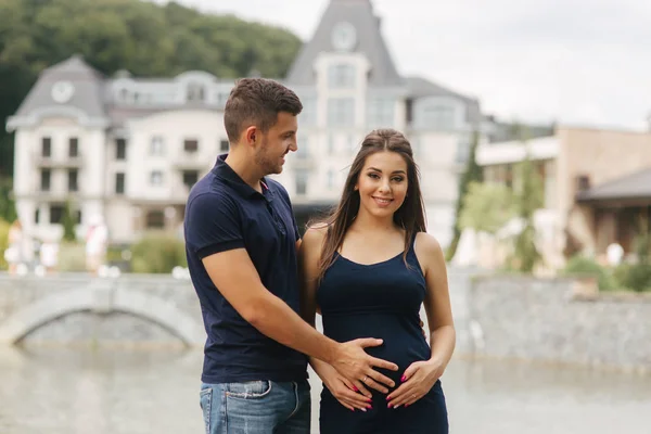 Schwangere und Ehemann umarmen sich und lächeln. Mann legte seine Hand auf Bauch einer schwangeren Frau. Sechs Monate Schwangerschaft — Stockfoto