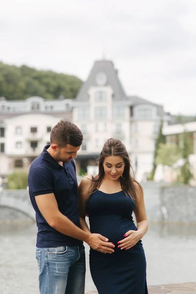 La mujer embarazada y su esposo se abrazan y sonríen. El hombre puso su mano de vientre de mujer embarazada. Seis meses de embarazo — Foto de Stock