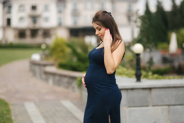Pregnant woman in dress holds hands on belly — Stock Photo, Image
