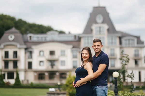 Schwangere und Ehemann umarmen sich und lächeln. Mann legte seine Hand auf Bauch einer schwangeren Frau. Sechs Monate Schwangerschaft — Stockfoto