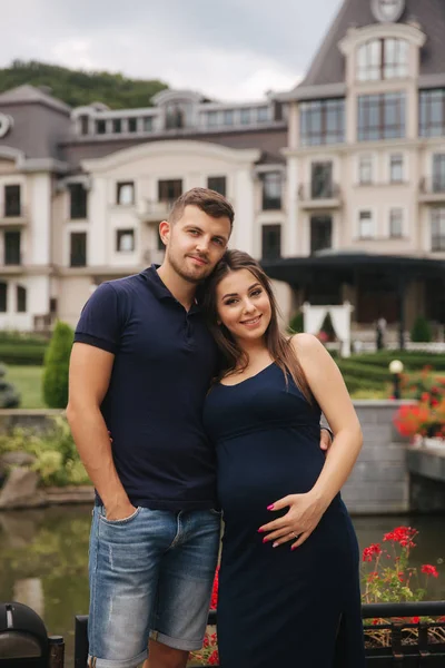 Schwangere und Ehemann umarmen sich und lächeln. Frau legte ihre Hand auf ihren Bauch. Sechs Monate Schwangerschaft — Stockfoto