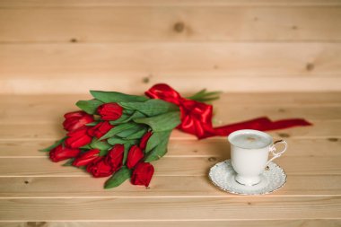 Güzel kırmızı lale ve lezzetli kapiçino ahşap zemin ile