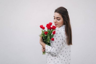 Çekici genç bayan beyaz gömlekli bir buket kırmızı çiçek tutun. Beyaz arka plan