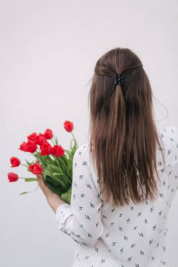 Çekici genç bayan beyaz gömlekli bir buket kırmızı çiçek tutun. Beyaz arka plan. Arkadan görünüm