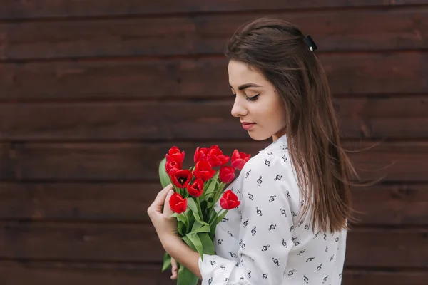 Chica joven con ramo de tulipanes rojos de pie fuera en frente de fondo de madera. Feliz hembra consiguió e ramo de flores — Foto de Stock