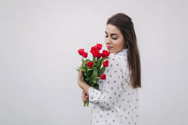 Приваблива молода леді в білій сорочці тримає букет червоних квітів. Білий фон — стокове фото
