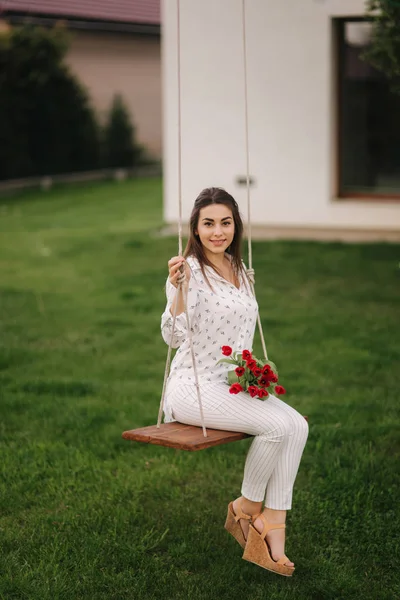 Леді в білому сидіти на гойдалки на задньому дворі свого будинку. Вона проведе re квіти — стокове фото