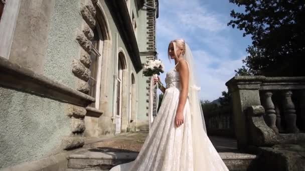 Geordeus bdire con elegante vestido de novia de pie en las escaleras con ramo de flores por el palacio — Vídeos de Stock