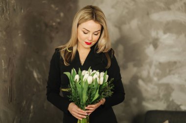 Güzel anne tutun 8 Mart Beyaz Lale bir buket. Kadının el çiçeklenir. Sarı saçlı anne ile evde çiçek