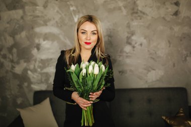 Güzel anne tutun 8 Mart Beyaz Lale bir buket. Kadının el çiçeklenir. Sarı saçlı anne ile evde çiçek