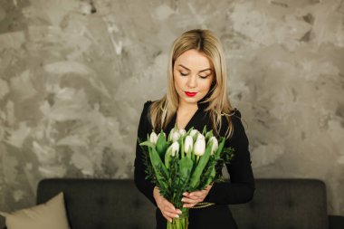 Güzel anne tutun 8 Mart Beyaz Lale bir buket. Kadının el çiçeklenir. Sarı saçlı anne ile evde çiçek