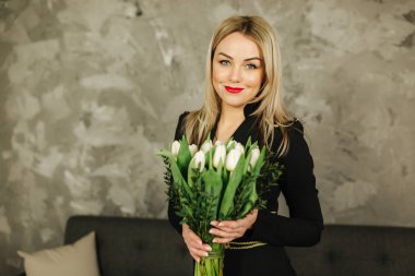 Güzel anne tutun 8 Mart Beyaz Lale bir buket. Kadının el çiçeklenir. Sarı saçlı anne ile evde çiçek