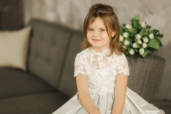 Retrato de menina bonita pouco segurar um buquê de flores em casa. Ela sist no sofá em casa e esperando por sua mãe. Buquê de flores no dia 8 de março. Presente — Fotografia de Stock