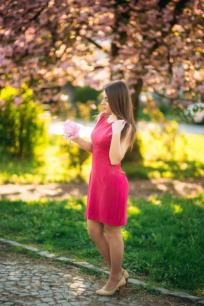 Mooi meisje poseren voor de fotograaf tegen de achtergrond van de bloei roze bomen. Lente. Sakura — Stockfoto