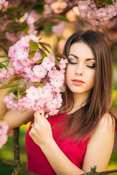 Retrato de una hermosa chica en sakura. Las flores de Sakura rodean a la chica. Sakura rama por su cara —  Fotos de Stock