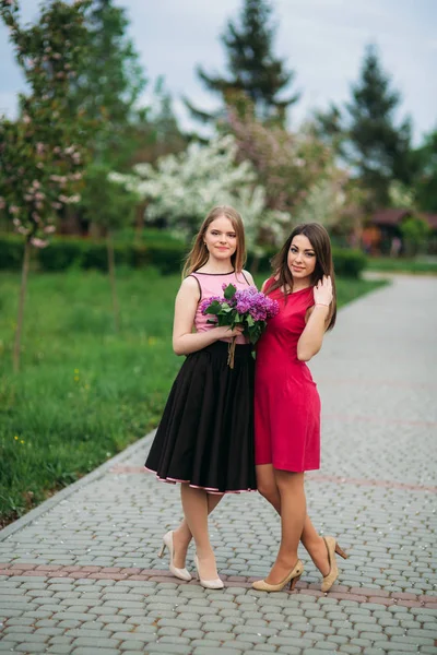 Två systrar som går utanför i vår park. De håller en bouqet av Syren och leende — Stockfoto