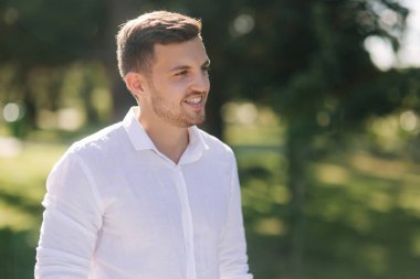 Beyaz bir gömlek ve şort gülümseme yakışıklı adam. Erkek model dışında. Park arka plan. Parkta yürüyen genç çekici adam