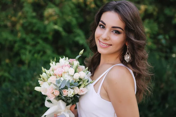 Hinreißende Frau im weißen Kleid Schleim. schönes Mädchen hält einen Blumenstrauß in den Händen — Stockfoto
