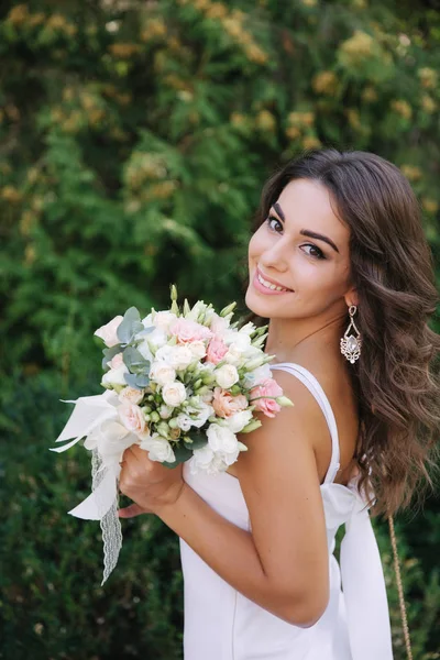 Hinreißende Frau im weißen Kleid Schleim. schönes Mädchen hält einen Blumenstrauß in den Händen — Stockfoto