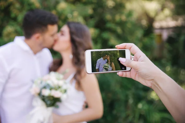 Quelqu'un prend une photo au téléphone pendant qu'ils s'embrassent. Beau couple en blanc — Photo