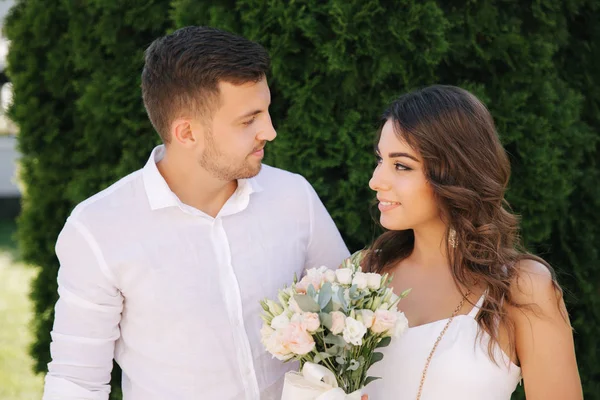 Schöner Mann und schönes Mädchen in weißen Kleidern. Paar zu Fuß nach draußen. Blumenstrauß — Stockfoto