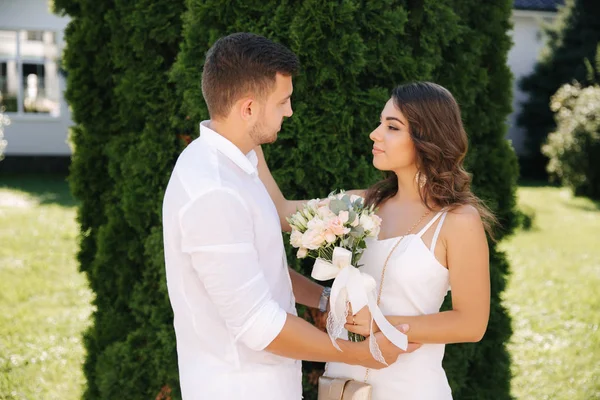 Schöner Mann und schönes Mädchen in weißen Kleidern. Paar zu Fuß nach draußen. Blumenstrauß — Stockfoto