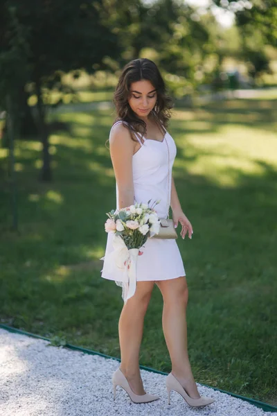 Элегантная женщина в красивом белом платье с букетом цветов прогуливается по парку. Женская модель снаружи — стоковое фото