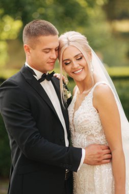 Yakışıklı damat güzel gelini sarıl. Parkta yürüyüş yeni evliler. Zarif gelinlik sarı saçlı kadın