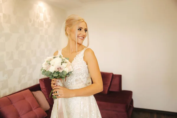 Noiva elegante em belo vestido de noiva com buquê em casa. Mulher de cabelo loiro com bela maquiagem e penteado — Fotografia de Stock