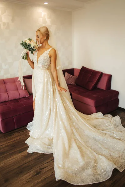 Élégante mariée dans une belle robe de mariée avec bouquet à la maison. Femme aux cheveux blonds avec beau maquillage et coiffure — Photo