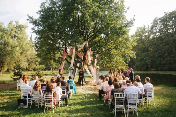 Свадебная церемония снаружи. Жених и невеста стоят у большого дерева. Декорации в парке. Фон озера — стоковое фото