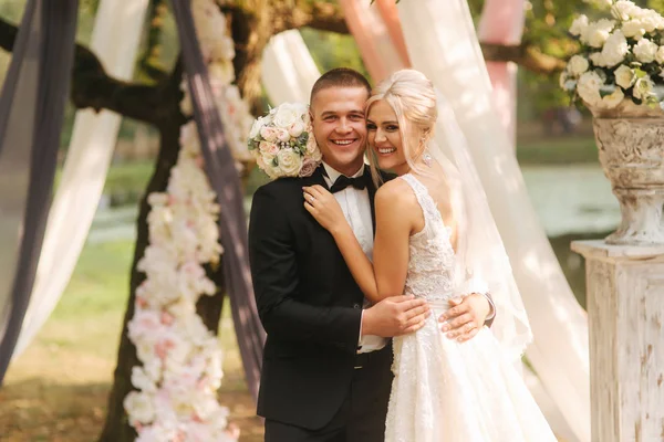 Cerimônia de casamento lá fora. Noivo e noiva ao pé da árvore grande. Decoração no parque. Contexto do lago — Fotografia de Stock