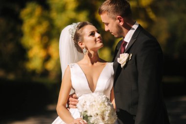 Güzel gelin kocası parkta. Sarı ağacın yanında yürüyorlar. Güzel makyaj