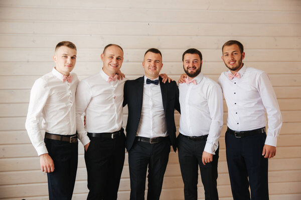 Handsome groom with his groomsman at home. Five man. Groom dressed in suit, gromsmen in white shirt. Funny guys on the wedding