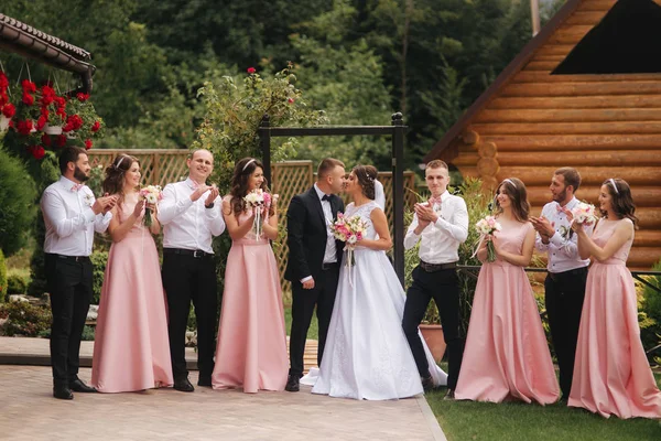 Ženich a nevěsta stojí s Družba a družička mimo. Novomanželé líbání a přítel tleskat. Svatební den — Stock fotografie