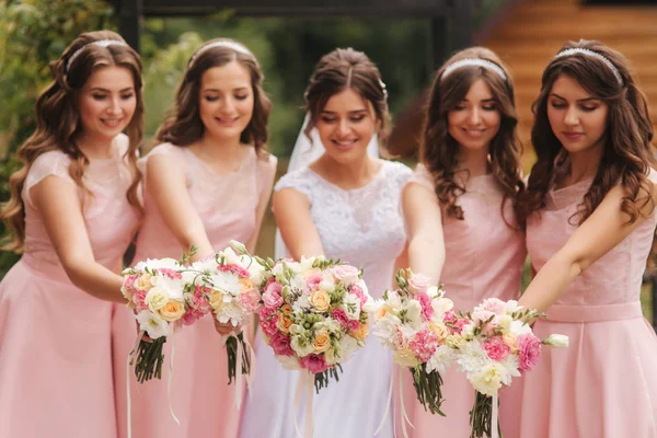 Glückliche Braut mit Brautjungfer halten Blumensträuße und haben Spaß draußen. schöne Brautjungfer in gleichen Kleidern stehen der charmanten Braut im langen Hochzeitskleid zur Seite — Stockfoto