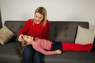 Anne ve kızı evde oynamak. Küçük kız annesi gıdıklıyor. Mutlu aile birlikte vakit geçirmek. Sarı saçlı kadın