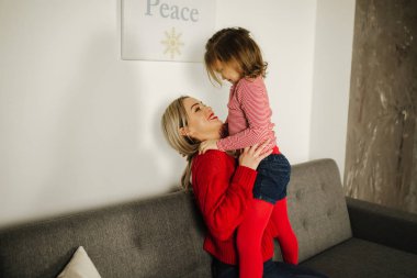 Anne kırmızı kazaklı ile küçük kız Kırmızı tayt giymiş. Evde mutlu bir aile. Kızın annesi sarılmak
