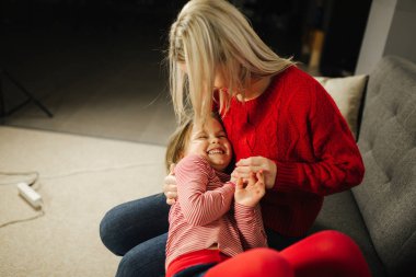 Anne ve kızı evde oynamak. Küçük kız annesi gıdıklıyor. Mutlu aile birlikte vakit geçirmek. Sarı saçlı kadın