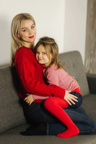 Fetiţă în colanţi roşii cu mama în pulover roşu. O familie fericită acasă. Fiica îmbrățișa mama ei — Fotografie, imagine de stoc