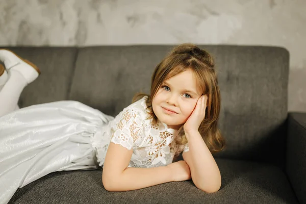 Μικρό κορίτσι σε λευκό φόρεμα στον καναπέ. Πέντε ετών κορίτσι στο σπίτι — Φωτογραφία Αρχείου
