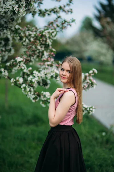 Bella ragazza dai capelli biondi in piedi davanti all'albero in fiore. Affascinante signora in abito — Foto Stock