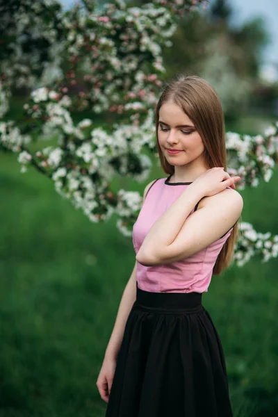 Bella ragazza dai capelli biondi in piedi davanti all'albero in fiore. Affascinante signora in abito — Foto Stock