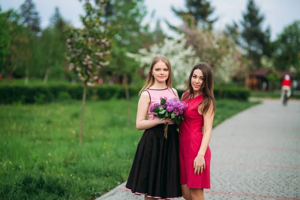 Zwei Schwestern, die draußen im Frühlingspark spazieren. sie halten einen Strauß Flieder und lächeln — Stockfoto