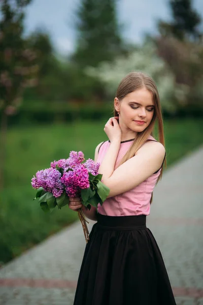 Attractive blond hair girl hold a bouquet of lilac in hands. Charming girl outside — Stock Photo, Image